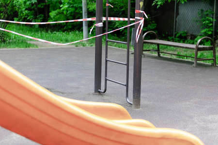 A slides at the children's playground in the park is wrapped with red barrier tape. Prohibition of outdoor walks, prevention of the coronavirus influenza virus covid-19. quarantine. selective focusの写真素材