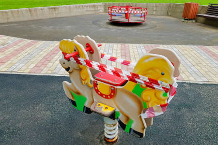 Children's toy on the playground wrapped with red barrier tape. Outdoors. Prohibition of outdoor walks, prevention of the biological hazard of the coronavirus influenza virus covid-19. state of alarmの写真素材