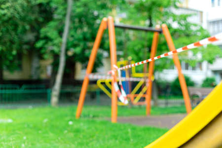 Children's playground on the grass in the park wrapped with red barrier tape. Prohibition of outdoor...
