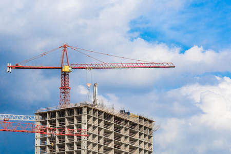 Several red cranes have been put to work on the construction of a modern multi-storey residential complex against a blue sky. Concept work for people with the profession of builder.の写真素材