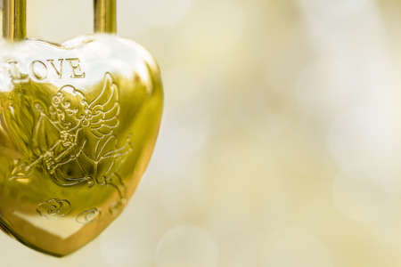 Hinged gold lock in the form of a heart, the inscription love angel with an arrow on a blurred background. Symbol of wedding. Copy space.の写真素材