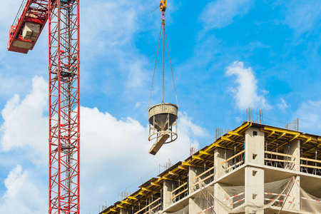 One high-rise crane with cement mortar against a house and blue sky during the construction phase. Industry concept for low-income young families. Mortgage, business, real estate loan.の写真素材