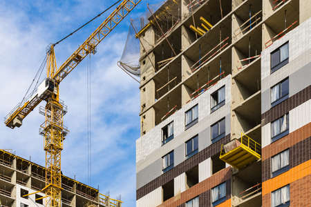 One yellow high crane against a house and sky during the construction phase. Industry concept for low-income young families. Mortgage, business, real estate loan. Summer. Daytime.の写真素材