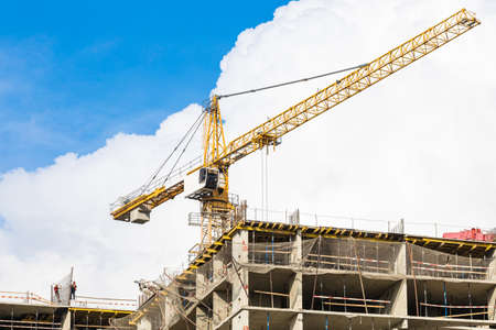 One yellow high-rise crane against a house and sky during the construction phase. Industry concept for low-income young families. Mortgage, business, real estate loan. Copy space.の写真素材