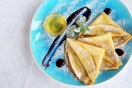 baked pancakes with mint honey powdered sugar and sauce on blue plateの写真素材