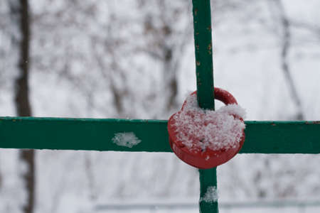 Red padlock covered with snow hanging on the bars as a sign of love