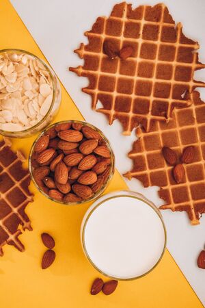 homemade waffles with almond nuts in the glass and almond chips and almond milk in the glass on the white and yellow background, copy space, top view, Making almond milk from dried almondsの写真素材