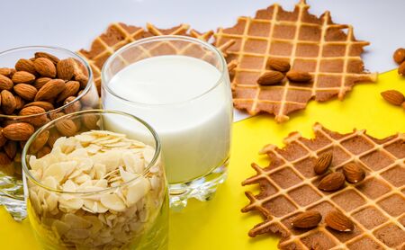 homemade waffles with almond nuts in the glass and almond chips and almond milk in the glass on the white and yellow background, copy space, top view, Making almond milk from dried almondsの写真素材
