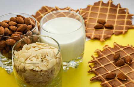 homemade waffles with almond nuts in the glass and almond chips and almond milk in the glass on the white and yellow background, copy space, top view, Making almond milk from dried almondsの写真素材