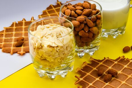 homemade waffles with almond nuts in the glass and almond chips and almond milk in the glass on the white and yellow background, copy space, top view, Making almond milk from dried almondsの写真素材