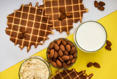 homemade waffles with almond nuts in the glass and almond chips and almond milk in the glass on the white and yellow background, copy space, top view, Making almond milk from dried almondsの写真素材