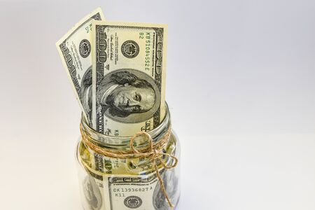one hundred american dollars in the jar on the white backround with copy space, savings, Many 100 US dollars bank notes in a glass jarの写真素材