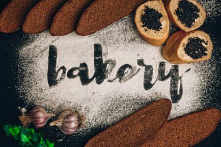 Inscription bakery on white wheat flour scattered Sliced rye bread with garlic and Tasty Sandwich with black caviar on dark background, hand written in flour the word bakeryの写真素材