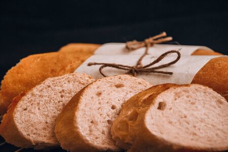 Sliced french baguette with crumbs on dark background, French homemade baguette bread. Wheat baguette on black shale, fresh tasty bread or baguetteの写真素材