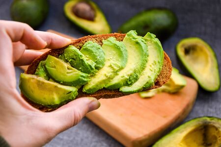 Healthy breakfast. Female hand holding Avocado toast, green organic avocadoの写真素材
