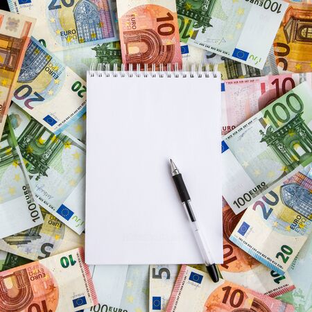 Opened spiral notepad sheet in a cage on money background, top view, copy space, A white notebook with blank pages lay on a set of banknotes of 100 euros, 50 euros, 20 euros 10 eurosの写真素材
