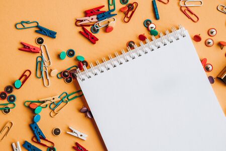 Office supplies of colored buttons and paper clips with empty note pad with copy space on yellow...