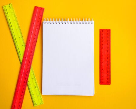 yellow and pink plastic ruler with empty notebook on the yellow background, copy space, back to...