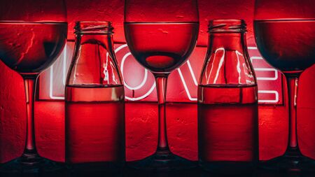 Set of different trensperent wine glasses and bottles on background with text LOVE with colorful multicolored light painting behind them, banner, alcohol drinksの写真素材