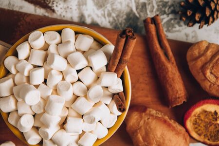 a cup of Christmas New Year delicious hot chocolate and cocoa with marshmallows sprinkled with cocoa powder on the wooden board, shape of spoon, dry orange slices, cones and croissants, cinnamon on a gray table, selective focus, hot drink winter or autumn top viewの写真素材