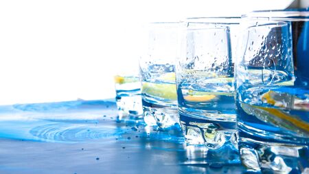 Line of Glasses of refreshing water with ice and lemon on a blue background. Heat concept, fresh. Natural light, copy space, summer hotの写真素材