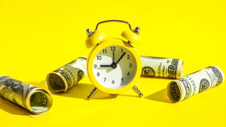 alarm clock both monetary denominations dollars, Time is money. Retro alarm clock and hundred dollar bills on a yellow background, The concept of the start of business investment, Banking, Savings, Wealthの写真素材
