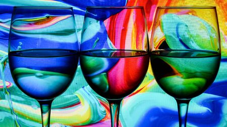 Three wine glasses in a row with colorful light painting behind, Set of three wine glasses with red, white and rose wine, banner, alcohol drinksの写真素材