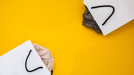 Paper craft package with purchases of womens clothing from which the linerie sticks out. On a bright yellow background. Black friday concept. Top view, flat lay, copy space, shopping bagの写真素材