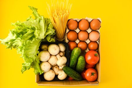 Groceries in paper box, basket with fresh vegetables and fruits on yellow background, freshly harvested vegetables, Gardening and healthy food conceptの写真素材