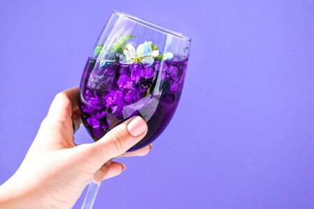 Close up of woman hand holding a glass full of cherry blossom flower or Sakura on purple background. Romantic traveling. Mother s day or womans day concept, copy space for textの写真素材