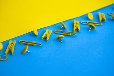 Office supplies in the form of colored buttons and paper clips, clothepins on yellow and blue background, copy space, border and frame, back to school concept of office chanceryの写真素材
