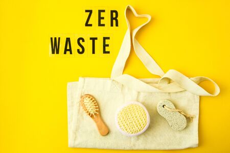 Zero waste concept. Textile eco bags, glass jars, wooden hair brush and washcloth on yellow background with Zero Waste black text in center. Eco friendly and reuse concept. Top view or flat layの写真素材