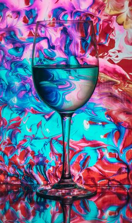 wine glass with colorful light painting behind, luxury splash drink in a glass on a high leg on a colored background, alcoholic drink bar conceptの写真素材