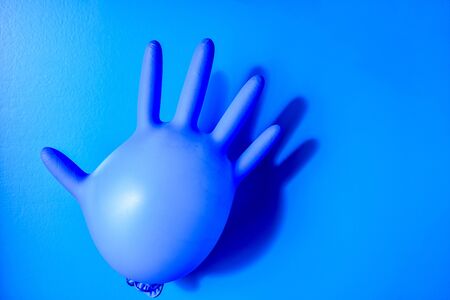 Blue latex medical glove on pastel blue backdrop. Minimal Coronavirus outbreak. Panic concept, copy space, Stay safe, quarantineの写真素材