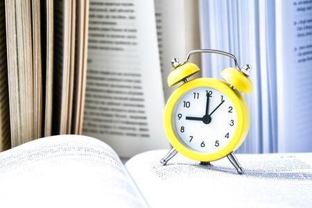 Yellow vintage alarm clock with book on white background, Back to school, Time to learn, wealth knowledge, copy space for textの写真素材