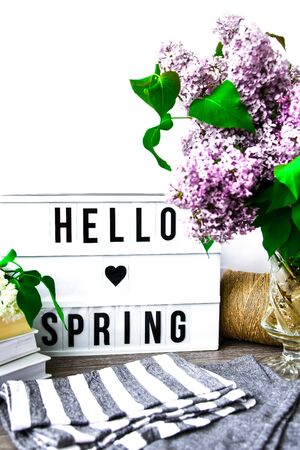 Lightbox with text GOOD MORNING and bouquet of violet lilac flowers in glass vase, spring time,...