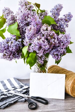 Lilac spring flower bouquet in glass vase on table with scissors and rope, copy space, holiday congratulation backgroundの写真素材