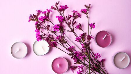 small pink flowers and aroma candles on pink background, copy space, skincare products, natural cosmetics for home spa treatment, holiday conceptの写真素材