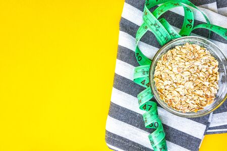 Oatmeal in a bowl and green centimeter tape on bright yellow background with kitchen towel, copy space, quick healthy breakfastの写真素材