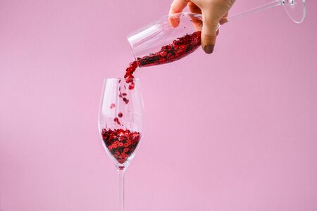 red confetti fall into champagne glass on pink background, copy space for text, creative holiday festive card, valentines dayの写真素材