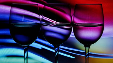 Three wine glasses in a row with colorful light painting behind, Set of three wine glasses with red, white and rose wine, banner, alcohol drinksの写真素材