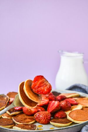 Plate with Traditional Pancakes and Tiny Pancake Cereal with Strawberries and Mint Leaves on a Dark Background. Trendy food. Selective focus on fork with tiny pancakes and strawberryの写真素材