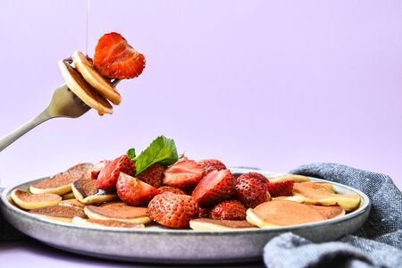 Selective focus on Maple syrup pouring on fork with tiny pancakes and strawberry. Pancake porridge,...