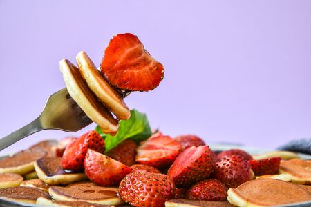Plate with Traditional Pancakes and Tiny Pancake Cereal with Strawberries and Mint Leaves on a Dark...