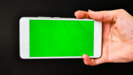 Young woman using white phone device with green screen. Woman holding phone. Chroma key. Close up....