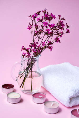 White cotton towel with small pink flowers and aroma candles on pink background, copy space, skincare products, natural cosmetics for home spa treatmentの写真素材