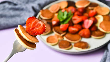Plate with Traditional Pancakes and Tiny Pancake Cereal with Strawberries and Mint Leaves on a Dark Background. Trendy food. Selective focus on fork with tiny pancakes and strawberryの写真素材