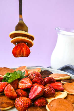 Plate with Traditional Pancakes and Tiny Pancake Cereal with Strawberries and Mint Leaves on a Dark Background. Trendy food. Selective focus on fork with tiny pancakes and strawberryの写真素材