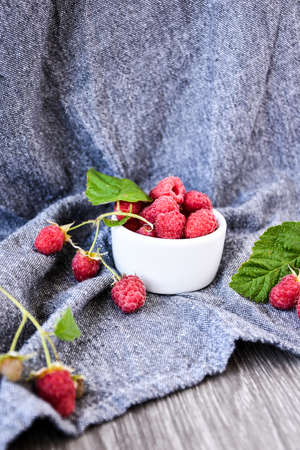 Ripe red raspberries in white bowl with green leaves on wooden background. Copy space. summertime fresh fruits.の写真素材