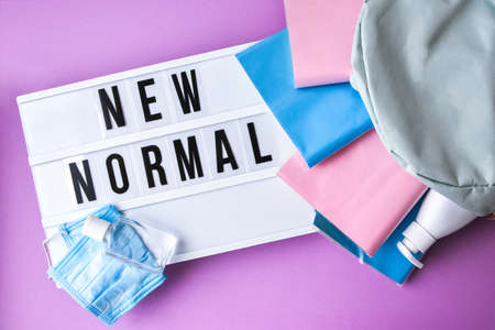 Lightbox with text NEW NORMAL protective face mask and sanitizer. Back to school. Books falling from backpack. Social distancing. Education in quarantine 2020の写真素材